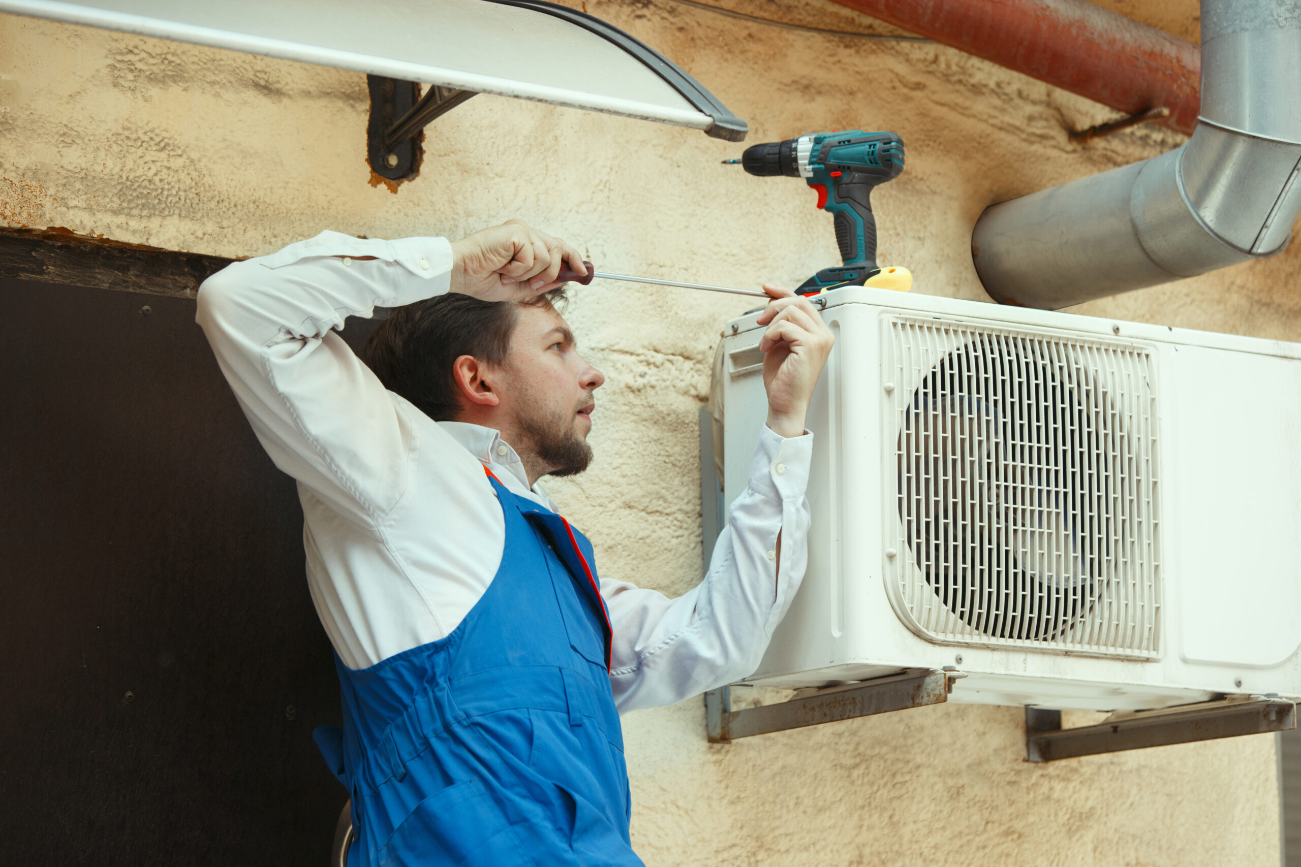 HVAC technician working on a capacitor part for condensing unit. Male worker or repairman in uniform repairing and adjusting conditioning system, diagnosting and looking for technical issues.